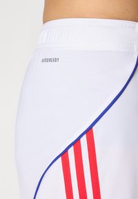 White athletic shorts with red vertical stripes and blue accents. Features an elastic waistband and the text “AEROREADY” on the back.