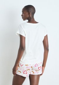 Camiseta blanca de manga corta combinada con pantalones cortos rosa claro que presentan un estampado juguetón de corazones y dachshunds. Tejido suave y liso.