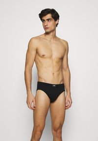 Slip nero con vita elastica, texture liscia e design minimale. Caratterizzato dalla vestibilità aderente e da un colore solido e semplice.