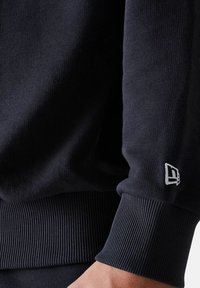 Felpa blu navy con polsini e orlo a costine, con un piccolo logo bianco sul polsino. Tessuto dalla texture liscia.