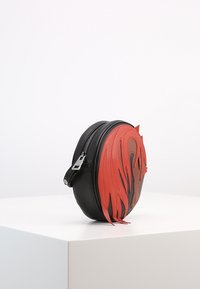 Borsa rotonda nera in pelle con design a fiamma rossa, chiusura a zip e tracolla regolabile. Texture liscia con accenti a strati distintivi.