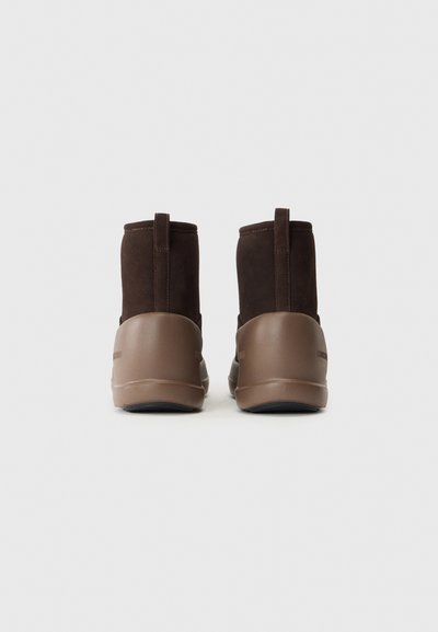 Ein Paar braune Winterstiefel mit Obermaterial aus Wildleder und Gummisohle, von hinten auf einem schlichten weißen Hintergrund betrachtet.