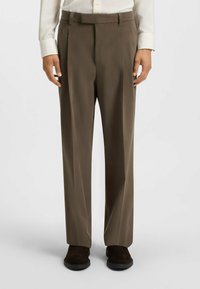Brown tailored trousers with pleats, made of smooth fabric. Pairs with a light-colored shirt and dark footwear. Straight cut design.