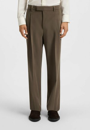Brown tailored trousers with pleats, made of smooth fabric. Pairs with a light-colored shirt and dark footwear. Straight cut design.