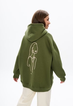 Olijfgroene oversized hoodie met een trekkoordkap. Kenmerkt een witte lijntekening van een gezicht op de achterkant. Zacht, gestructureerd materiaal.