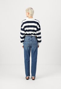 Sweater às riscas brancas e azul-marinho com um corte solto, combinado com jeans azuis de cintura alta com bainhas desfiadas e bolsos traseiros.