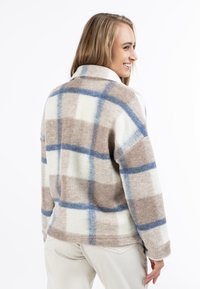 Geruite trui in crème, bruin en blauw. Zachte, pluizige textuur met een kraag en een ontspannen pasvorm. Heeft een groot ruitpatroon.