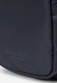 Borsa a spalla in tessuto blu navy con una texture sottile. Presenta il logo "Marc O'Polo" stampato in grigio, che accentua il design minimale.