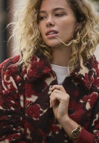 Kurtka z polaru z kwiatowym wzorem w kolorach bordo i beżowym, zapinana na zamek, o miękkiej fakturze, z kontrastującymi bordowymi mankietami.