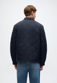 Μονωμένο μπουφάν σε ναυτικό μπλε χρώμα με ίσια γραμμή, γιακά με αιχμηρή μορφή και μακριά μανίκια. Κατασκευασμένο από λείο ύφασμα με ματ φινίρισμα.