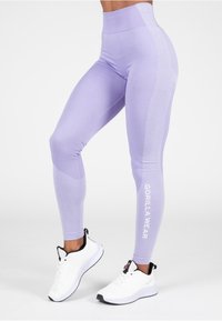 Lavender sportleggings met textuurpanelen aan de zijkanten en het witte "GORILLA WEAR" logo, gecombineerd met witte sneakers met zwarte accenten.