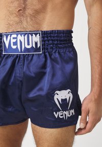 Tamsiai mėlyni satino bokso šortai su elastinga juosta, puošti baltais siuvinėtais "VENUM" logotipu ir gyvatės dizainu. Sklandus tekstūra, laisvas kirpimas.
