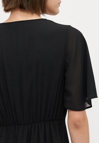 Black dress with a fitted waist and flared short sleeves. Made of light, sheer fabric, featuring a smooth, flowing texture.
