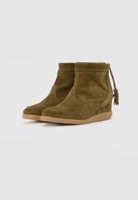 Bottines en daim vert avec un motif texturé, un col doux et une semelle en caoutchouc flexible, ornées d'un gland décoratif à l'arrière.