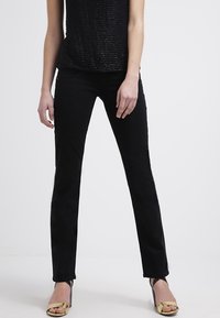 Black trousers with a slim fit, constructed from smooth fabric, featuring a flat front and slight stretch for comfort. Paired with gold-accented heels.