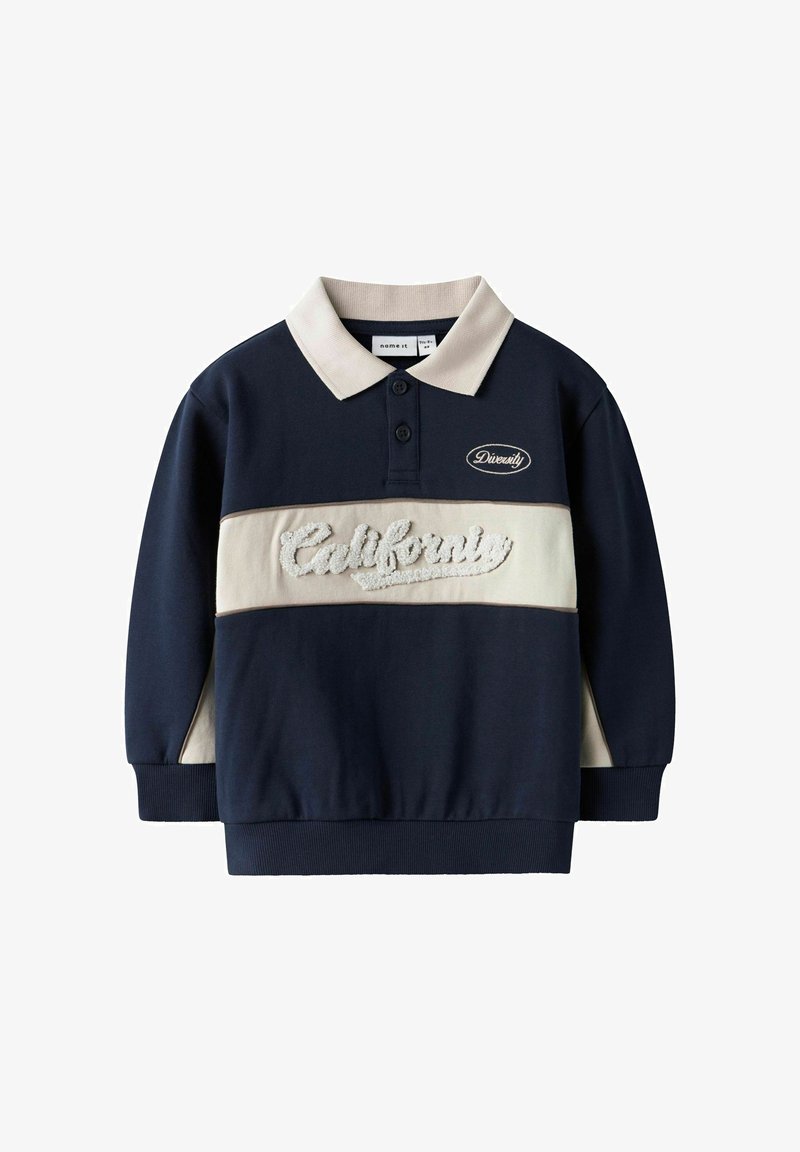 Felpa blu navy con una fascia orizzontale crema e ricamo testurizzato con la scritta "California". Presenta un colletto polo e polsini a costine.