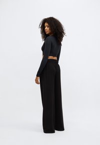 Melnas garām piedurknēm saīsināts tops kopā ar melnām biksēm ar platām kāju daļām. Gluda tekstūra, pieguļošs tops un elastīga jostasvieta biksēm.