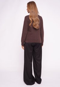 Brązowy, miękki sweter o luźnym kroju, zestawiony z czarnymi spodniami o szerokich nogawkach. Sweter ma prążkowany dół i mankiety.