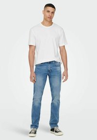 White cotton t-shirt paired with light blue denim jeans. The jeans have a straight cut and subtle fading, complemented by black sneakers.
