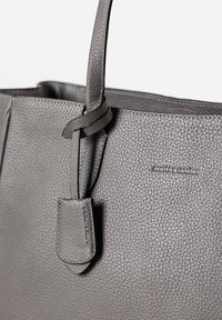 Borsa a mano in pelle grigia con una superficie texturizzata, manici robusti e un piccolo tag con logo impresso. Design semplice e funzionale.