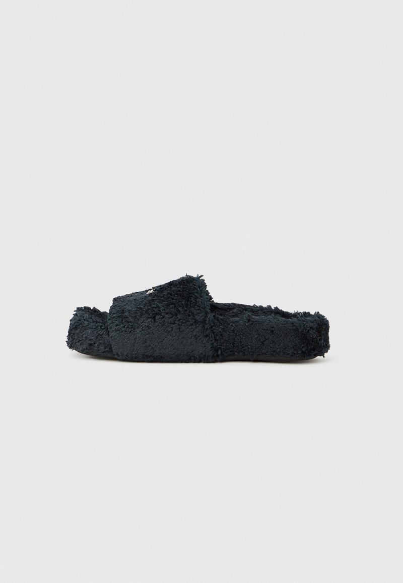 Juoda pūkuota atvira pirštų šlepetė su plačia juosta ir plokščiu padais, rodoma iš šono ant paprasto fono.