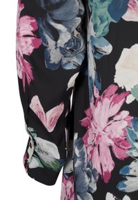 Manche en tissu noir avec un grand imprimé floral rose, bleu, blanc et vert, montrant un poignet froncé avec des boutons noirs.