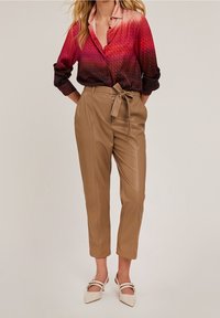 Långärmad skjorta i gradient röd och rosa med ett mönstrat textur, tillsammans med högmidjade, beige avsmalnande byxor med ett knytbälte.