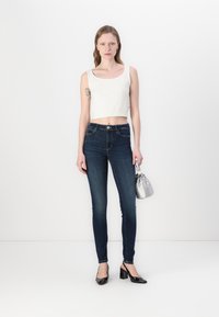 White sleeveless crop top, dark blue skinny jeans, black patent heels, and a small silver handbag. Smooth textures and fitted design.