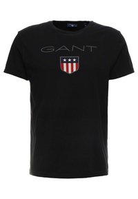 Camiseta negra de manga corta con el logotipo de GANT y un emblema de escudo que presenta tres estrellas blancas sobre rayas verticales rojas y blancas.