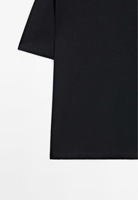 Sort kortærmet skjorte med ren sømkant mod en hvid baggrund, der viser venstre side og nederste kant af tøjet.