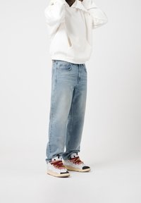 White hooded sweatshirt, light blue denim jeans, and multicolored sneakers with black and cream accents. Casual fit, no visible patterns.