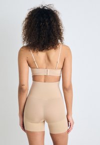 Șorturi bej modelatoare cu talie înaltă și bretele ajustabile, realizate dintr-un material neted și elastic, cu un design fără cusături și cusături minime.