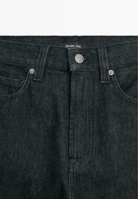 Jeans in denim scuro con una trama liscia, dotati di hardware argentato, design a cinque tasche e etichetta del marchio sulla vita.