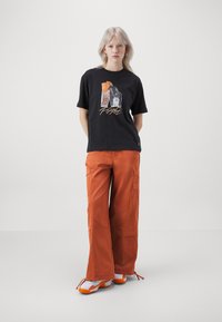 Black graphic t-shirt with a basketball print and orange accents, paired with orange wide-leg cargo pants featuring pockets and a loose fit.