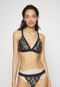 Biquíni triangular com padrão de estampado de leopardo, com alças e acabamentos pretos. O tecido parece liso, com texturas contrastantes e um design de faixa na cintura.