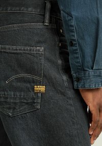 Jans oscuros de mezclilla con un acabado texturizado, que presentan una etiqueta dorada de G-Star, un bolsillo trasero cosido y un ajuste ligeramente entallado.