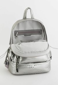 Srebrny plecak z nylonu o zaokrąglonym kształcie, z przednią kieszenią na zamek, akcentami na sznurku oraz wyściełanymi ramiączkami. Gładka faktura z eleganckim wykończeniem.