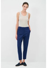 Marineblauwe tailorpantalon met een slim-fit, voorzakken en een gladde textuur. Gecombineerd met een lichtbeige geribbeld tanktop en marineblauwe instappers.