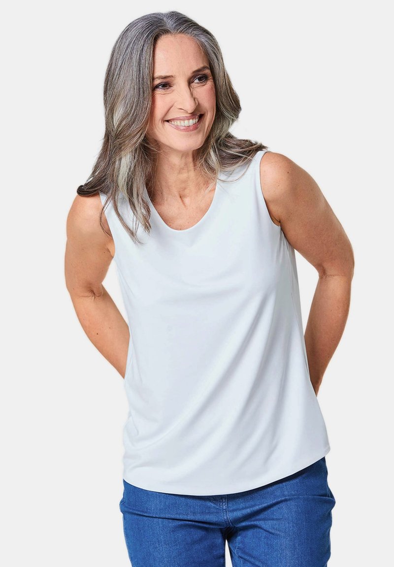 Witte mouwloze top met een ronde halslijn, gemaakt van een soepele stof, met een ontspannen pasvorm en subtiele draping, gecombineerd met blauwe jeans.