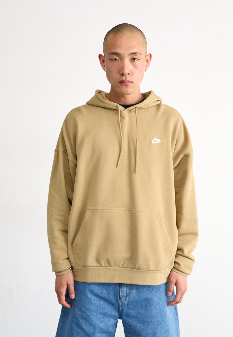 Sweat-shirt beige avec capuche, doté d'une poche avant et d'un petit logo blanc. Coupe décontractée, porté avec un jean en denim ample. Texture lisse.