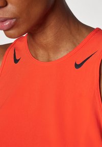 Czerwony bezrękawnik sportowy z okrągłym dekoltem, z czarnymi logo Nike na każdym ramieniu i gładką fakturą materiału.