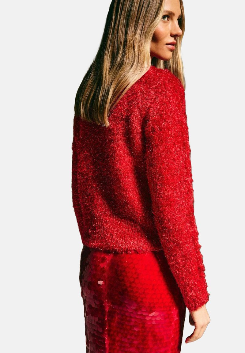 Sweater rouge en peluche avec un col rond et des manches longues, associé à une jupe rouge pailletée brillante créant un contraste texturé.