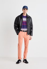 Black leather jacket, striped purple and grey shirt, peach-colored pants, black shoes with white stripes, blue cap.