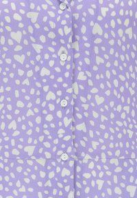 Levandulová košile na knoflíky s bílým vzorem srdcí a teček, se pěti bílými knoflíky vpředu. Hladká látka s lehkou texturou.