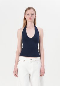 Navy haltertop gemaakt van zachte stof met een V-hals ontwerp. Gecombineerd met losse witte jeans, voorzien van een knoop en metalen accenten.