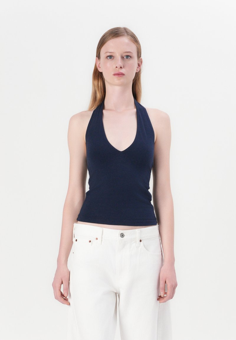 Navy haltertop gemaakt van zachte stof met een V-hals ontwerp. Gecombineerd met losse witte jeans, voorzien van een knoop en metalen accenten.