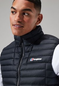 Zwarte gewatteerde vest met opstaande kraag, ritssluiting en Berghaus-logo. Gestructureerd oppervlak met horizontale stiknaad en een gladde afwerking.