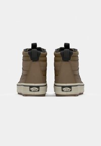 Baskets montantes marron avec des panneaux texturés, des accents noirs, des semelles en caoutchouc et des languettes à l'arrière. Logo Vans sur le talon.