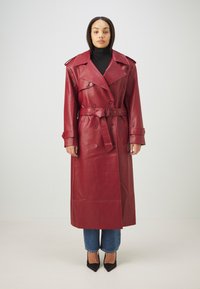 Rød læder trenchcoat med dobbeltbrystet front, brede klapper og en bælte i taljen; parret med blå jeans og sorte spidse hæle.