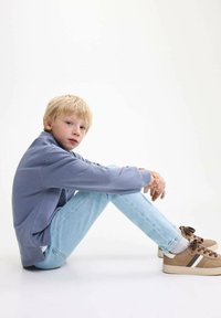 Svetlo modrý mikina, svetlo modré džínsy a hnedé tenisky s bielymi a tmavohnedými akcentmi. Dieťa sedí s prekríženými nohami.